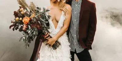 A bride and groom posing in a studio setting with smoke effects, the bride wearing a white floral dress and holding a bouquet.