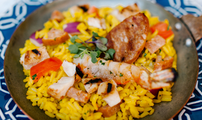 A close-up of a plated dish featuring yellow rice, shrimp, sausage, and vegetables.