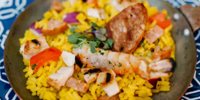 A close-up of a plated dish featuring yellow rice, shrimp, sausage, and vegetables.