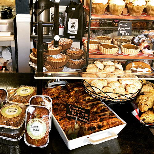A display case at Mimi's Plate filled with various baked goods, pies, and pastries, including cinnamon rolls and pumpkin cake.