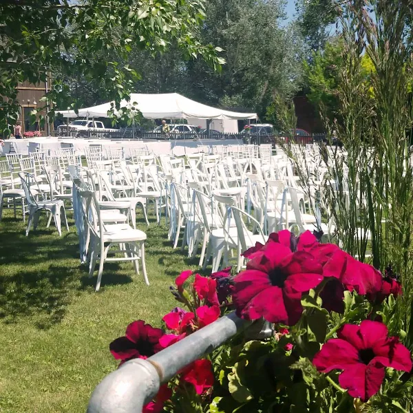 Outdoor wedding venue with rows of white chairs on a lawn, a white tent, and a rustic building in the background.