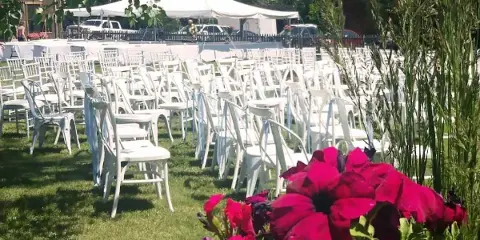 Outdoor wedding venue with rows of white chairs on a lawn, a white tent, and a rustic building in the background.