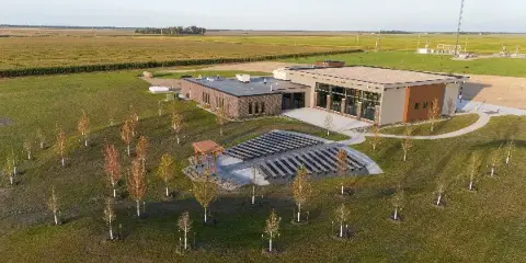 Aerial view of a modern event venue building with outdoor seating area and landscaped grounds in a rural setting.