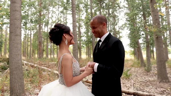A bride and groom holding hands and smiling at each other in a forest setting.
