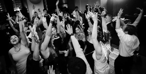 A black and white photo of a crowded wedding dance floor with guests raising their hands and dancing.