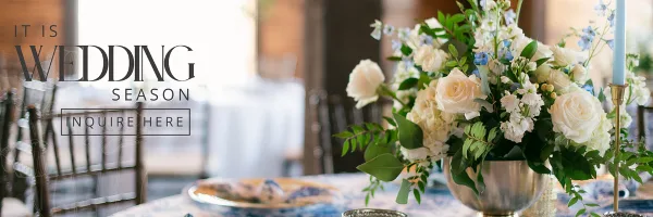 A floral arrangement with white roses and greenery in a silver vase on a table.