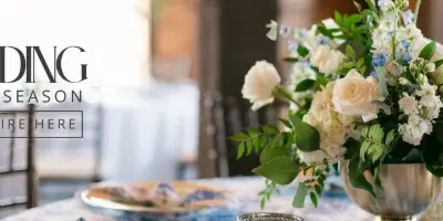 A floral arrangement with white roses and greenery in a silver vase on a table.