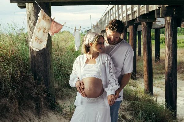 A professional portrait of a couple standing together outdoors near a wooden pier structure.