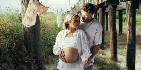 A professional portrait of a couple standing together outdoors near a wooden pier structure.