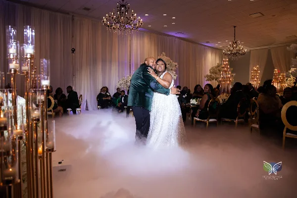 A bride and groom dancing at a wedding reception in a ballroom with chandeliers and floor fog.