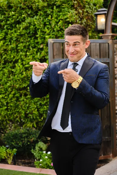 A man in a blue suit and tie pointing at the camera.