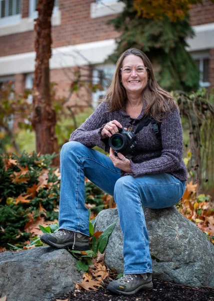 A woman sitting on a rock outdoors holding a professional camera.