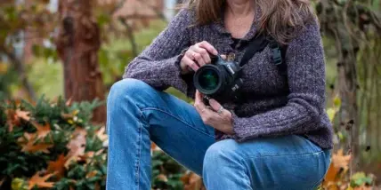 A woman sitting on a rock outdoors holding a professional camera.