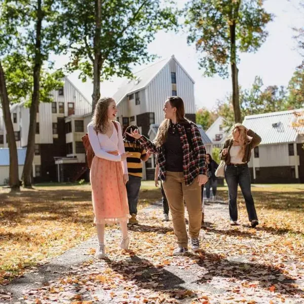 Students walking on a path in front of a white barn-style building on a college campus.