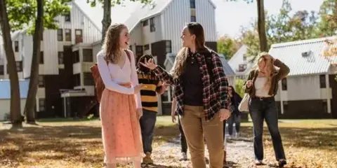 Students walking on a path in front of a white barn-style building on a college campus.