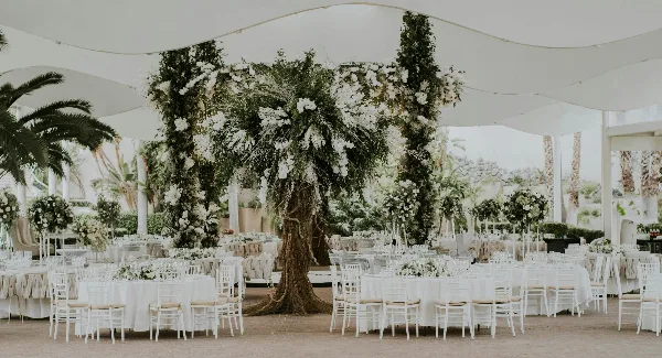 A wedding reception venue featuring a large floral archway, white Chiavari chairs, and round tables with white linens.