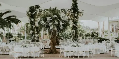A wedding reception venue featuring a large floral archway, white Chiavari chairs, and round tables with white linens.
