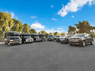 A lineup of luxury SUVs and party buses parked in a lot under a blue sky.