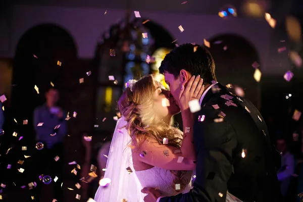 A bride and groom share a first dance at a wedding reception while confetti falls and colored event lights illuminate the background.