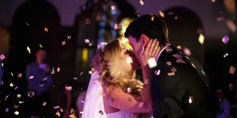 A bride and groom share a first dance at a wedding reception while confetti falls and colored event lights illuminate the background.