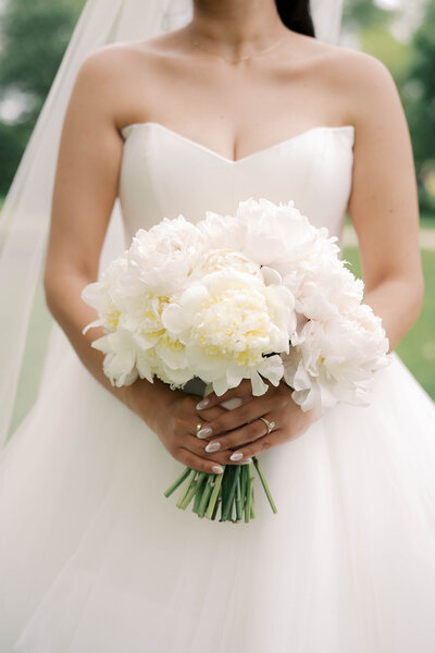 A bride in a white gown holding a large bouquet of white and ivory peonies.