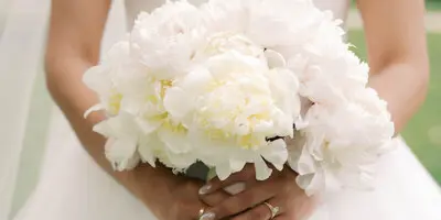 A bride in a white gown holding a large bouquet of white and ivory peonies.