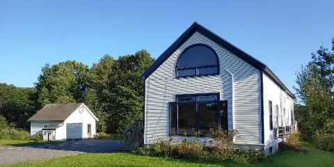 Exterior view of a white community center building with a large arched window and a smaller garage-like structure, set on a grassy lawn.