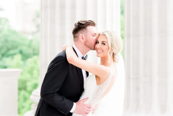 A bride and groom sharing a kiss in front of white architectural columns.