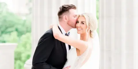 A bride and groom sharing a kiss in front of white architectural columns.