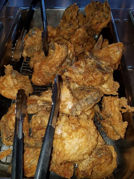 Buffet tray of golden fried chicken pieces with serving tongs