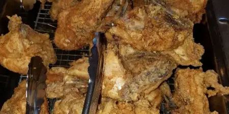 Buffet tray of golden fried chicken pieces with serving tongs