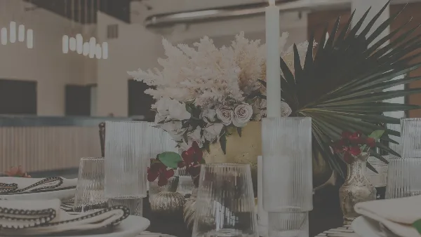 A close-up of a decorated event table featuring white floral arrangements, tall candles, and glassware in a modern venue setting.