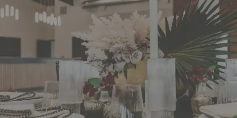 A close-up of a decorated event table featuring white floral arrangements, tall candles, and glassware in a modern venue setting.