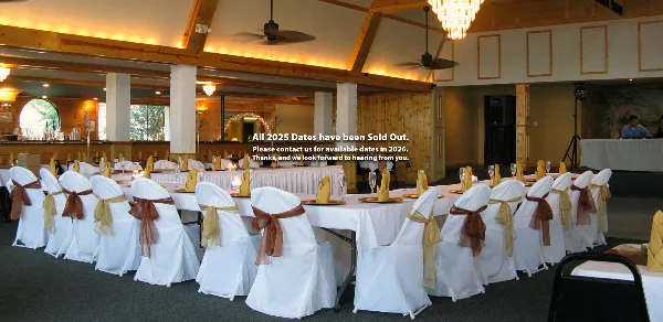 Interior view of a wedding reception hall with long tables, white chair covers, and wooden beams.