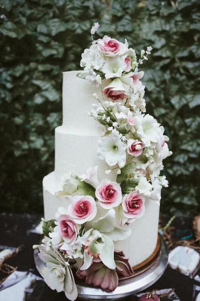 A three-tiered white wedding cake decorated with cascading pink and white sugar flowers.