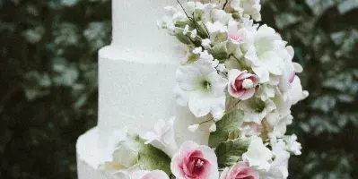 A three-tiered white wedding cake decorated with cascading pink and white sugar flowers.
