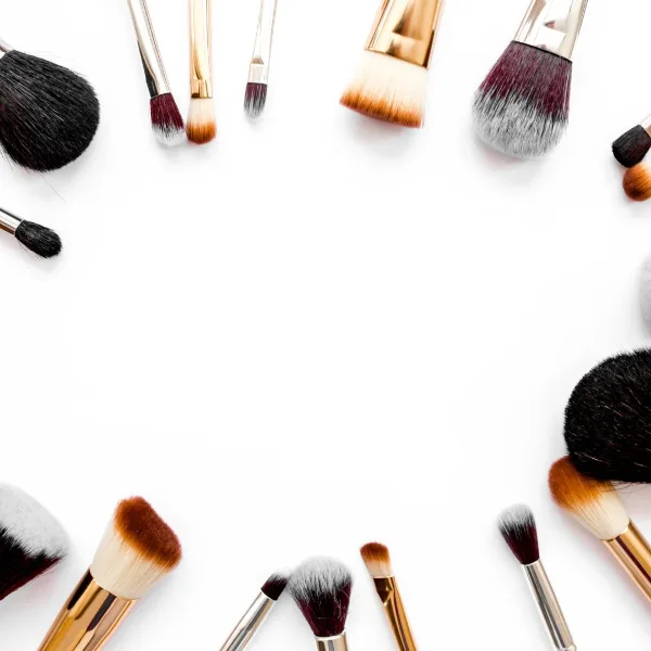 An assortment of professional makeup brushes with gold handles arranged around a white background.