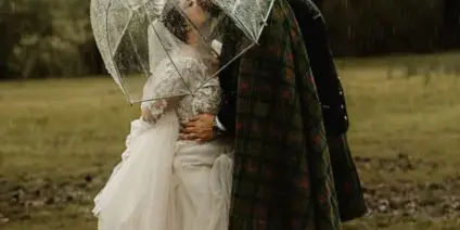 A bride and groom sharing a kiss under a clear umbrella in a misty, wooded field.