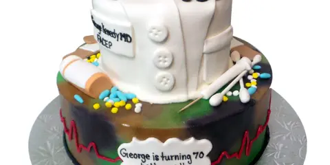 A two-tier custom cake shaped like a doctor's coat with a stethoscope and medical tools, sitting on a silver cake stand with a branded card.