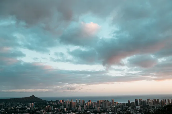 Wide cinematic view of the Honolulu skyline and Diamond Head under a dramatic cloudy sky.