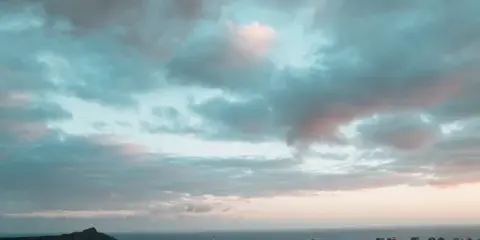 Wide cinematic view of the Honolulu skyline and Diamond Head under a dramatic cloudy sky.