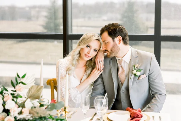 A bride and groom posing together at a table with floral arrangements and candles.