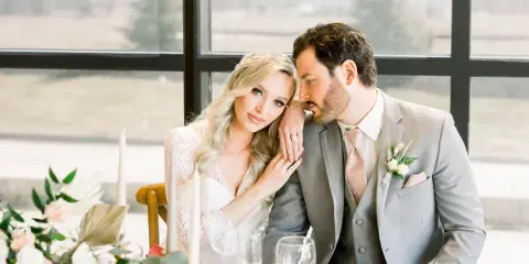 A bride and groom posing together at a table with floral arrangements and candles.