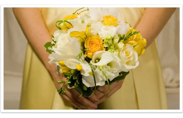 A person in a yellow dress holding a bouquet of white calla lilies and yellow roses.