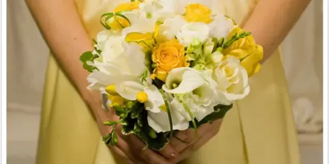 A person in a yellow dress holding a bouquet of white calla lilies and yellow roses.
