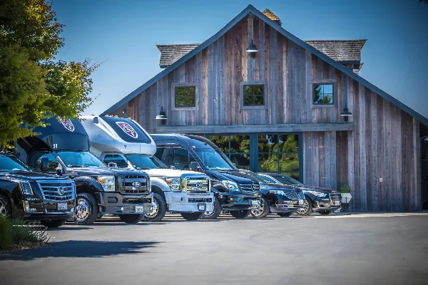 A fleet of luxury limousines, party buses, and sedans parked in front of a rustic wooden building.