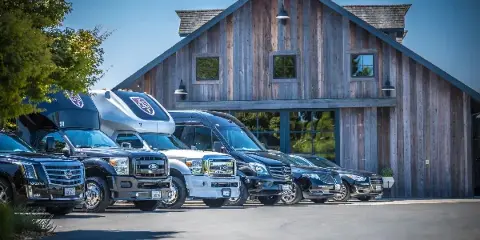 A fleet of luxury limousines, party buses, and sedans parked in front of a rustic wooden building.