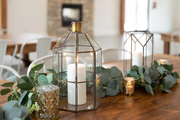 Wedding table decorated with gold lanterns, white candles, mercury glass votives, and eucalyptus greenery.