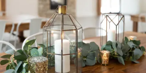 Wedding table decorated with gold lanterns, white candles, mercury glass votives, and eucalyptus greenery.