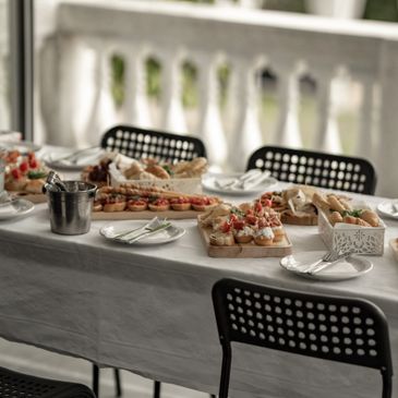 A long table set with a white tablecloth, displaying an assortment of appetizers, bread, and plated food ready for a catering event.
